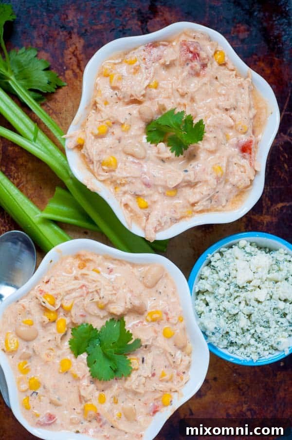 Two steaming bowls of creamy buffalo chicken chili are shown, garnished with fresh celery sticks and crumbled blue cheese, ready to be enjoyed.