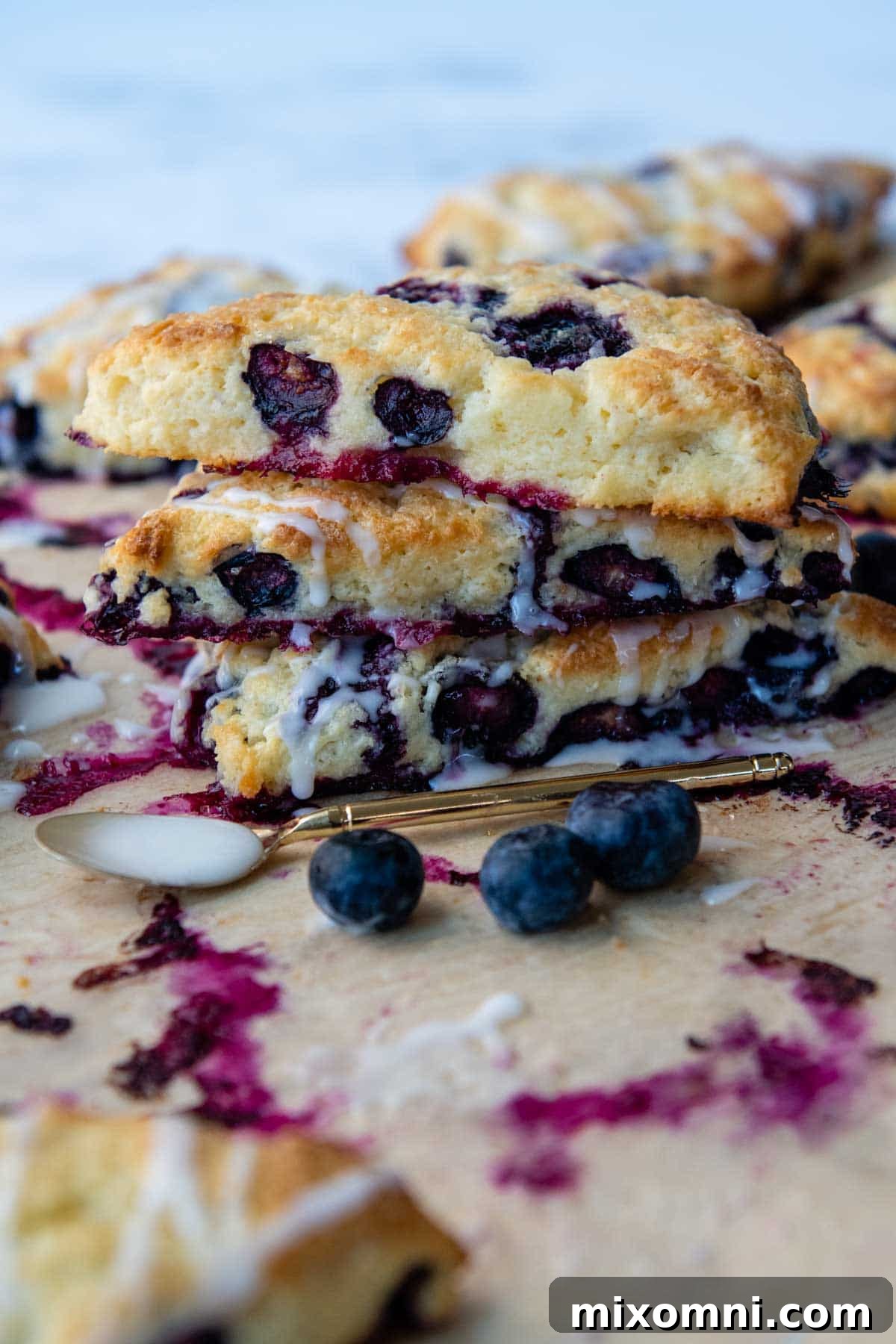 A stack of golden-brown gluten-free blueberry scones, drizzled with glaze, with fresh berries scattered around.