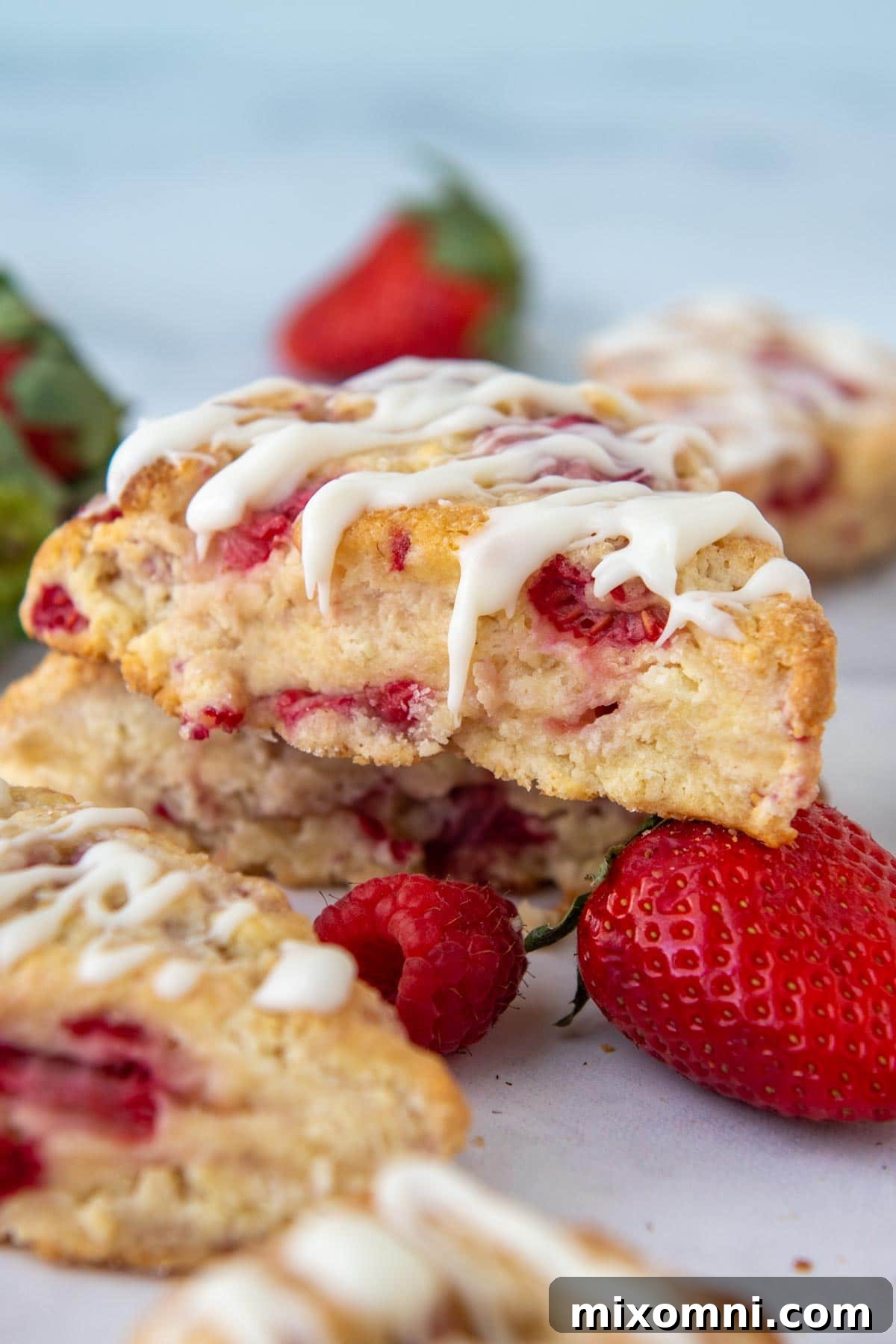 A beautifully glazed strawberry and raspberry scone resting delicately on a fresh strawberry.