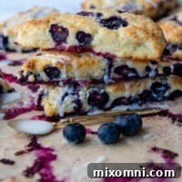 A stack of perfectly baked gluten-free blueberry scones with fresh berries scattered around.