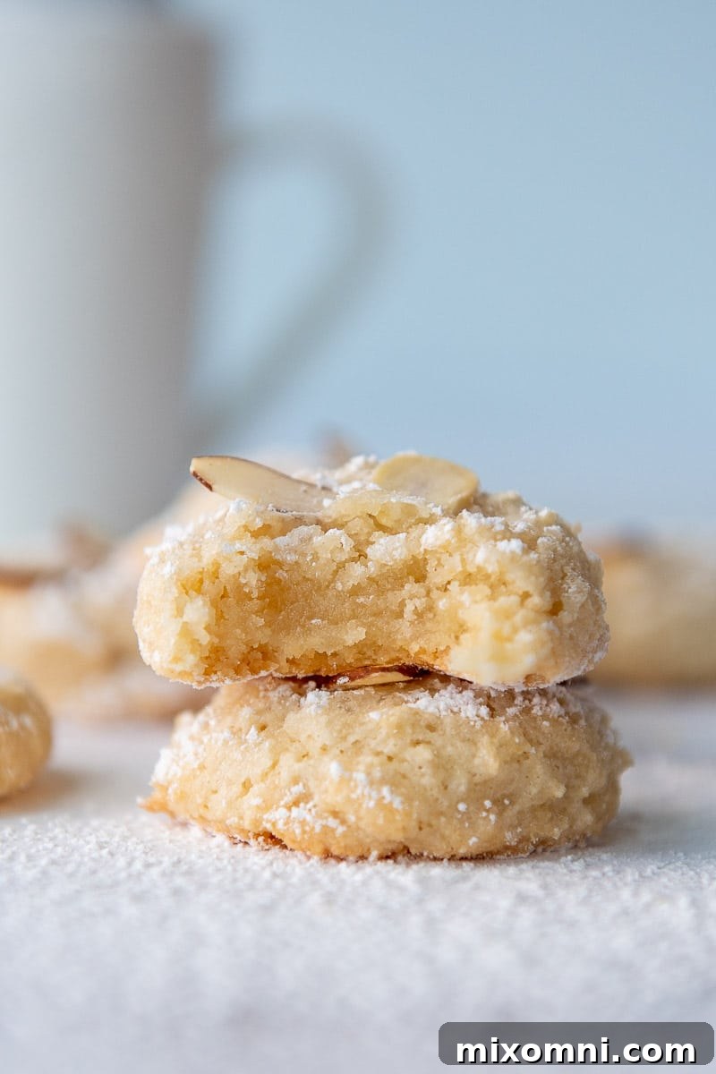 A stack of two perfectly baked Italian Almond Paste Cookies, with a tantalizing bite taken out of the top one, showcasing its soft interior.