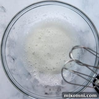 A beaten egg white in a glass bowl, prepared to the perfect frothy consistency.
