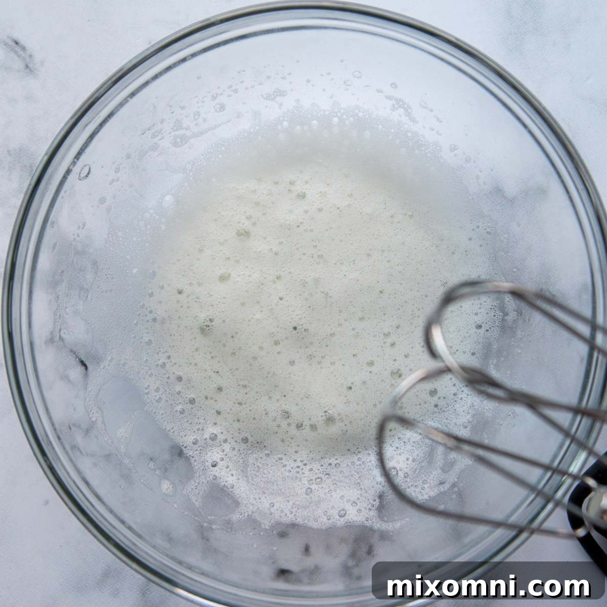 Egg whites briefly beaten until frothy and opaque in a clear glass bowl, ready for the next step of mixing.