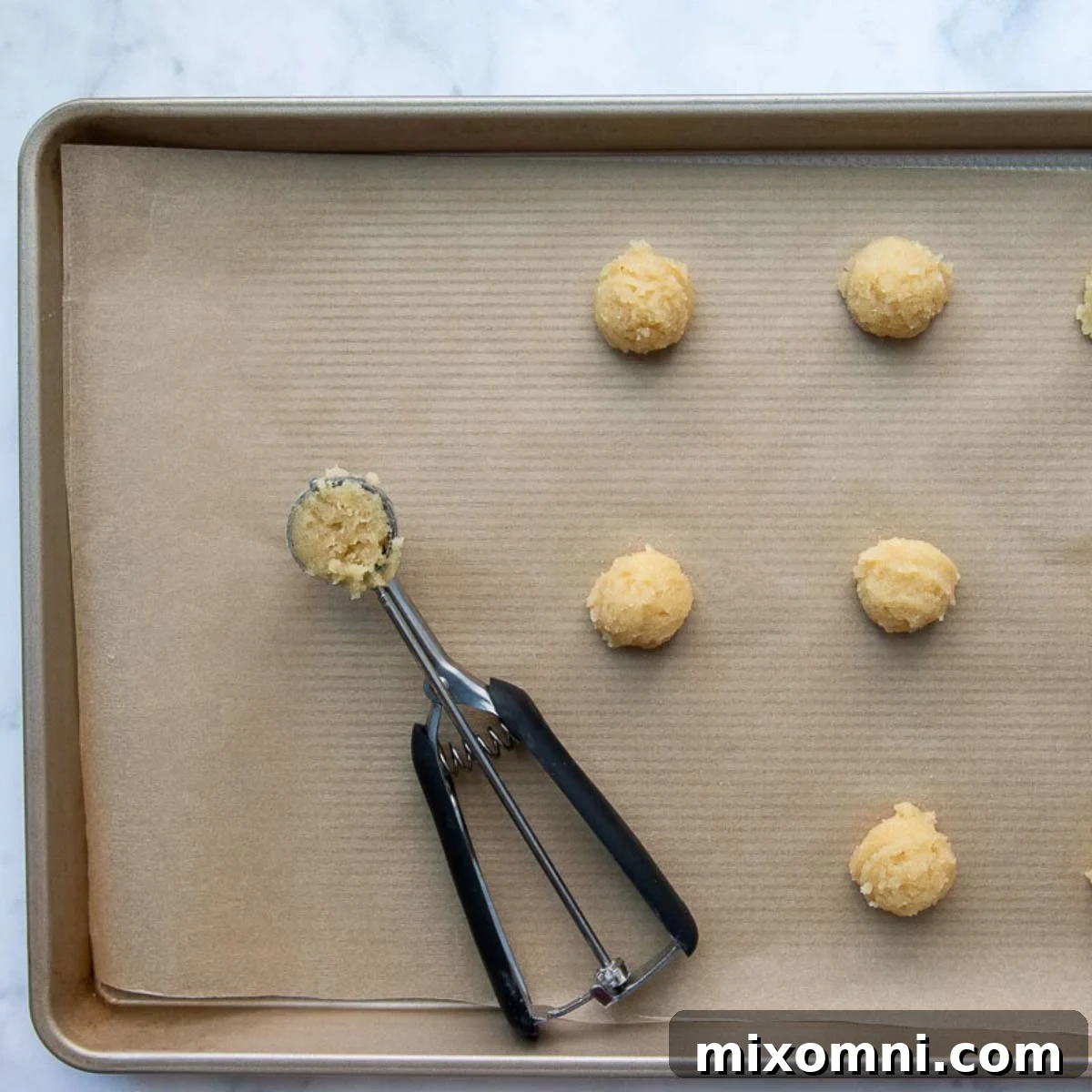 Perfectly portioned cookie dough balls on a baking sheet, precisely measured with a cookie scoop, ready for baking.