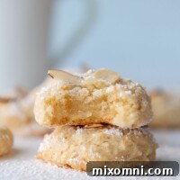 A stack of two beautifully baked Italian almond paste cookies, with a tempting bite taken out of the top cookie, revealing its soft interior.