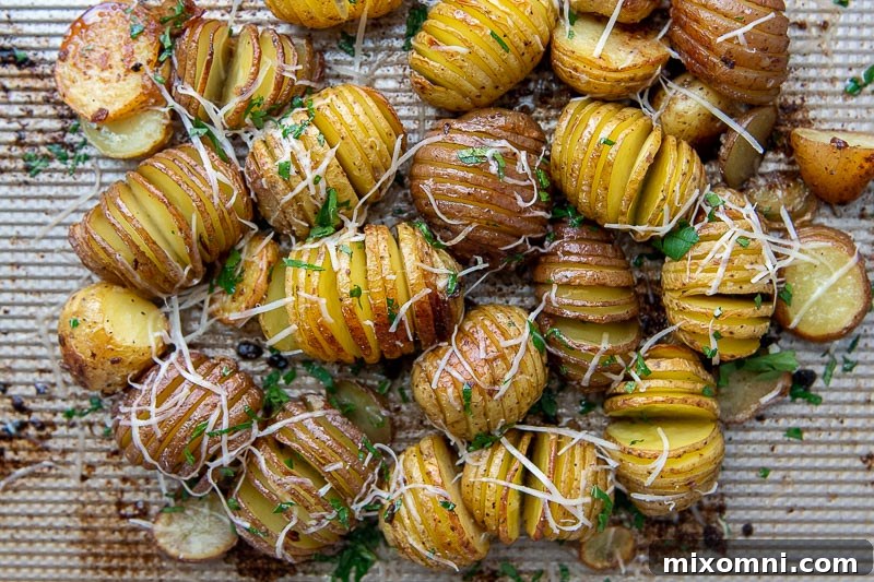 Mini Hasselback potatoes on a baking sheet, fresh out of the oven, with melted Parmesan cheese on top.