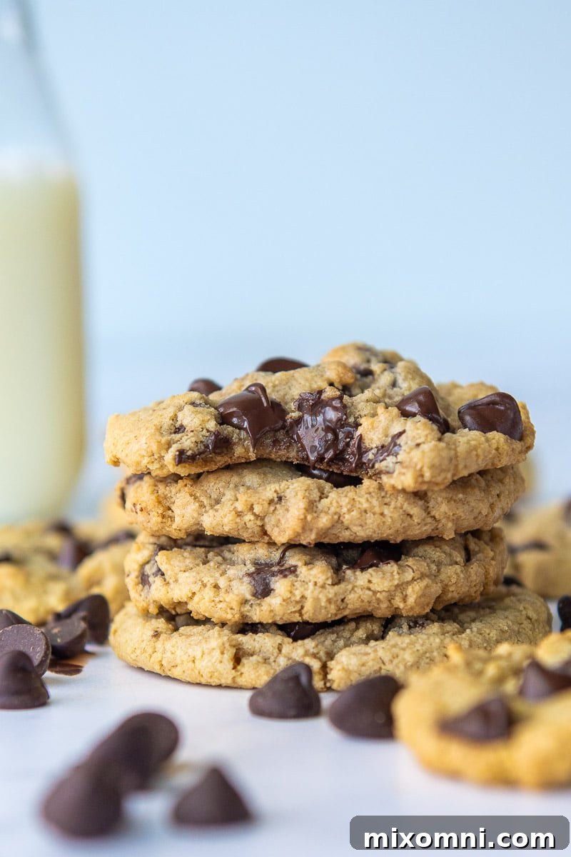 A tempting stack of golden-brown oat flour cookies, with the top one showing a perfect bite mark revealing its soft, chocolatey interior.