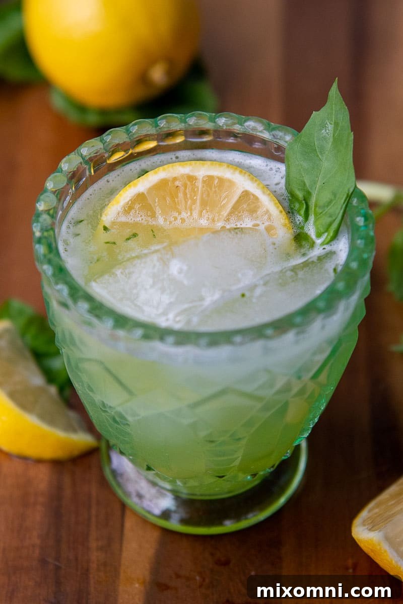 A vibrant Gin Basil Smash cocktail in a green glass, garnished with a lemon wedge and fresh basil leaves, ready to be enjoyed.