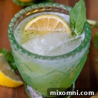 a gin basil smash cocktail in a green glass with a lemon wedge and basil garnish