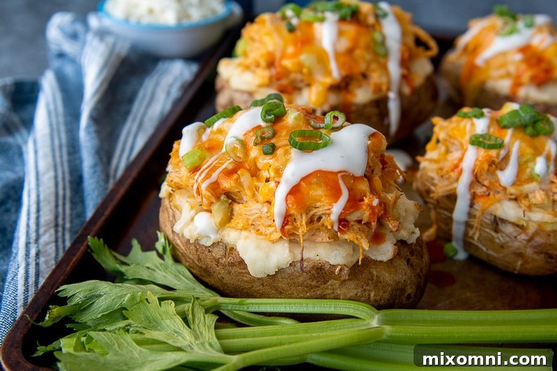 A twice-baked potato, beautifully stuffed with spicy buffalo chicken and melted cheese, resting on a baking sheet, with fresh celery sticks and a side of dressing, highlighting its fresh components.