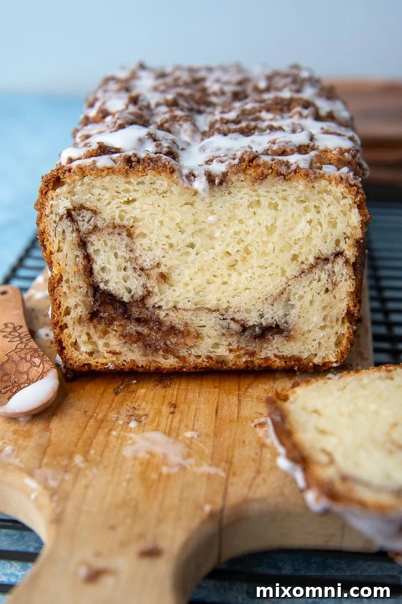A slice of gluten-free cinnamon bread on a cutting board, generously topped with vanilla glaze.