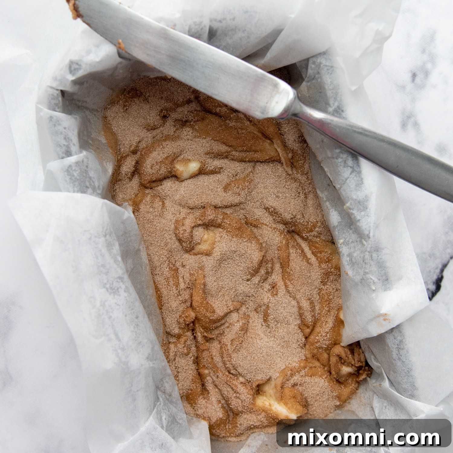 Layers of bread dough and cinnamon sugar mixture in a loaf pan, ready for swirling.