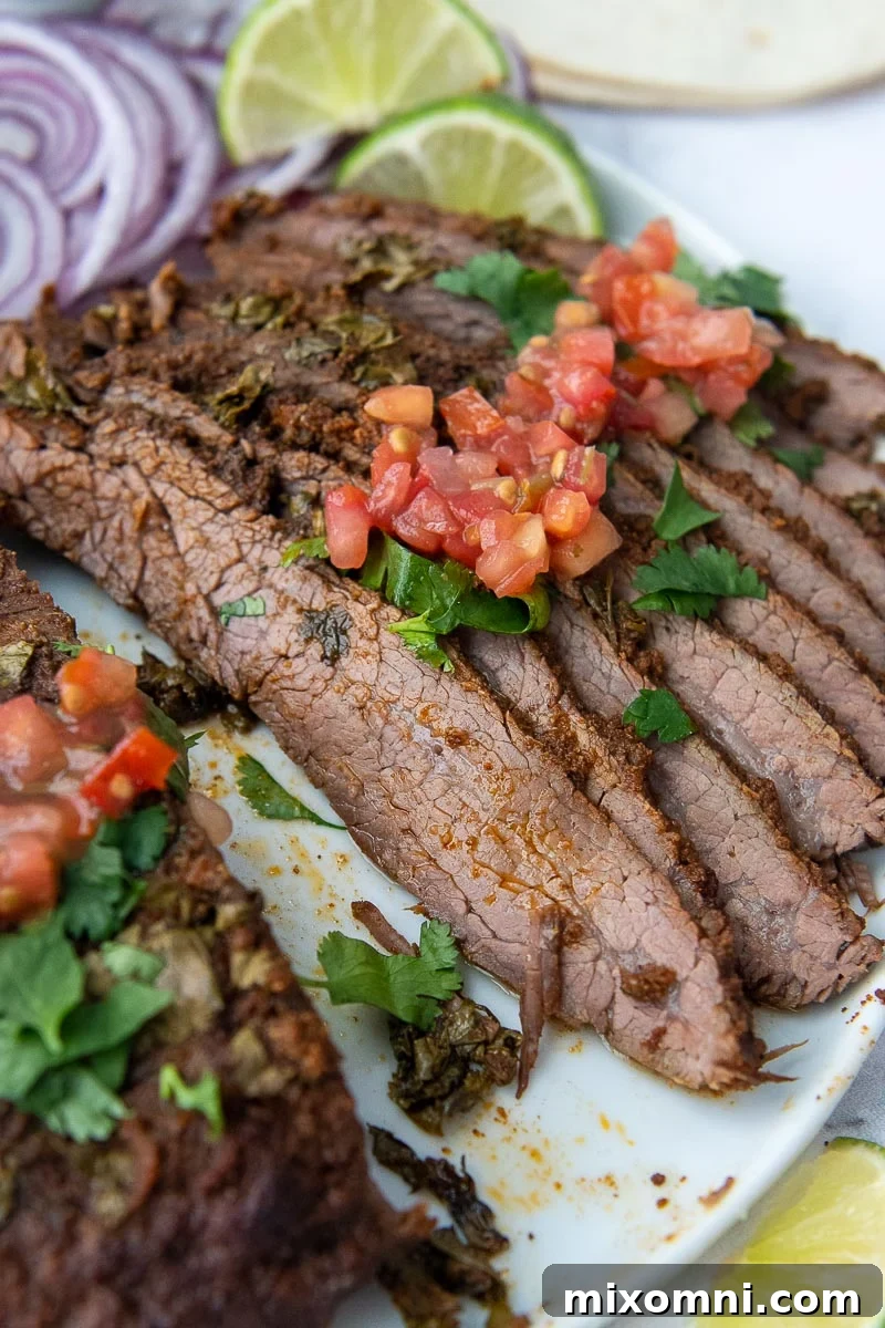 Sliced flank steak on a plate, generously topped with fresh pico de gallo, ready to serve.