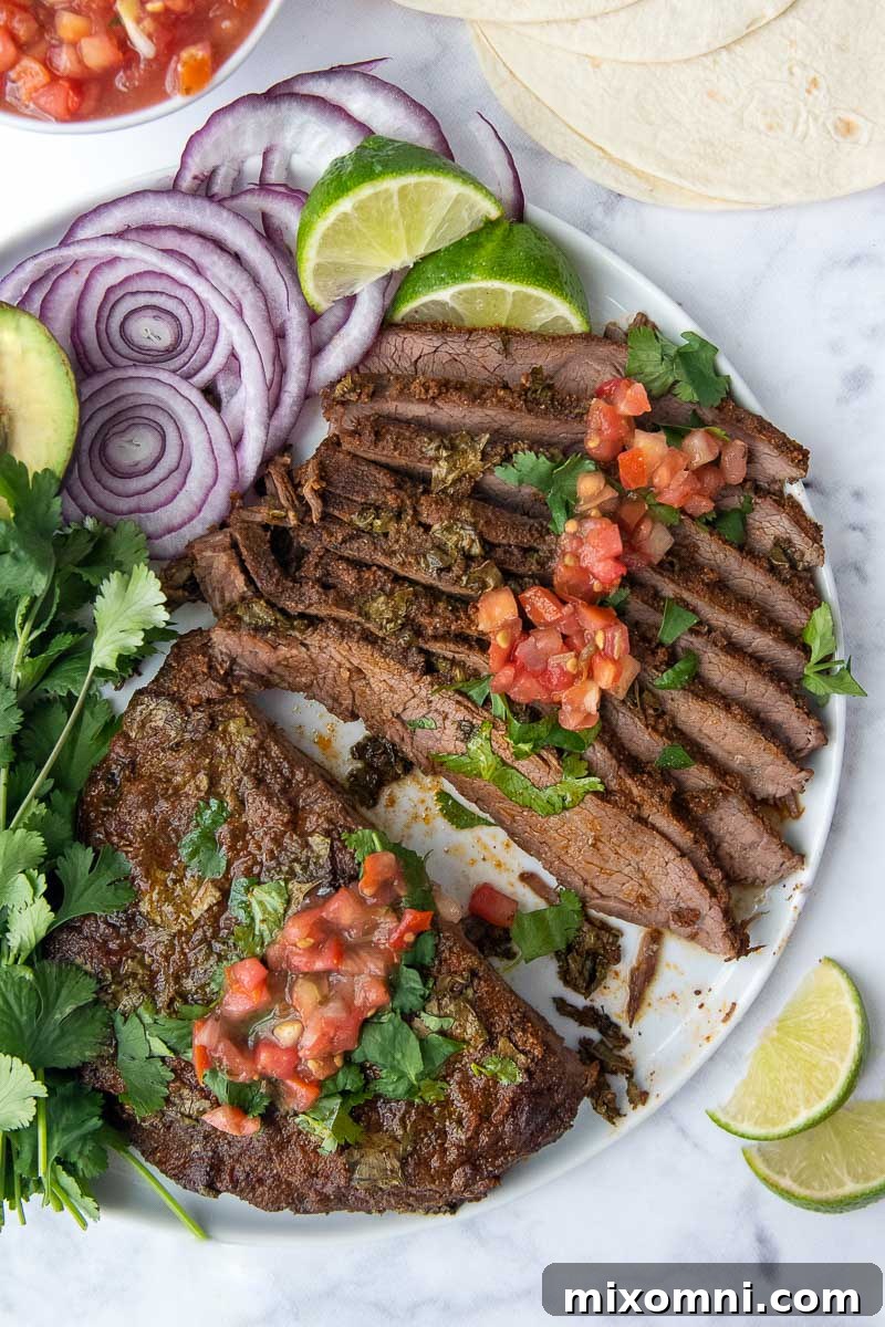 Overhead shot of perfectly sliced carne asada, garnished with avocado, red onion, and lime wedges.