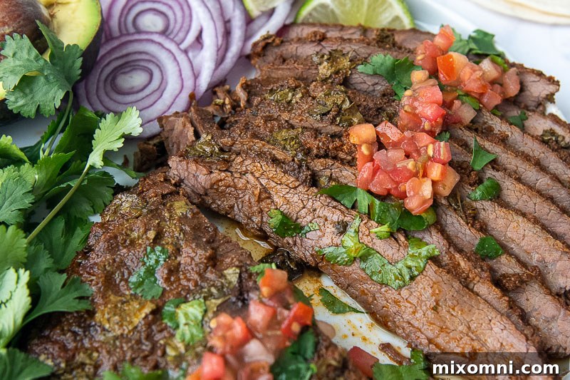Close-up shot of perfectly sliced flank steak on a white plate, garnished with fresh herbs.
