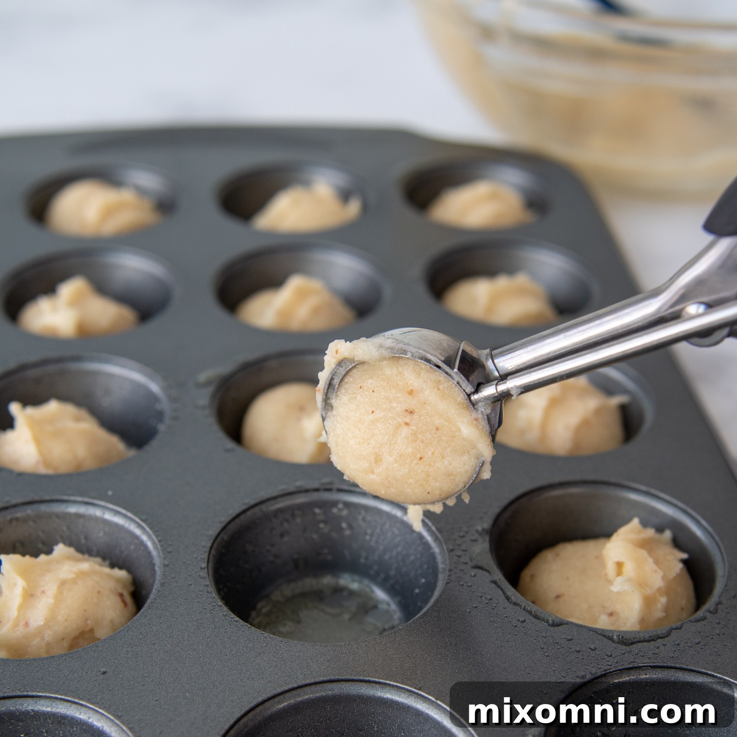 a small scoop putting the dough in a mini muffin pan.