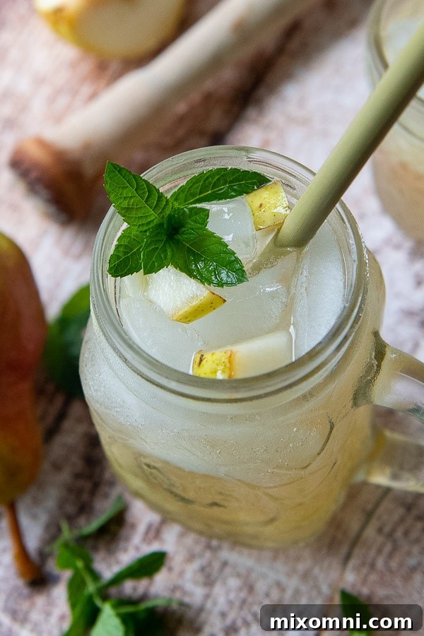 A top-down view of a ginger cocktail, garnished with fresh pear slices and mint leaves, glistening in the light.