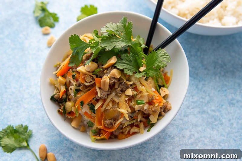 A white bowl filled with the Unstuffed Egg Roll Bowl, served over rice, with chopsticks placed on the side.