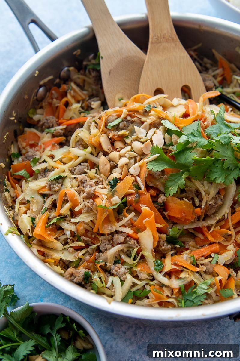 Close-up shot of the finished Unstuffed Egg Roll Bowl still in the skillet, with wooden cooking utensils sticking out, highlighting its delicious texture and ingredients.