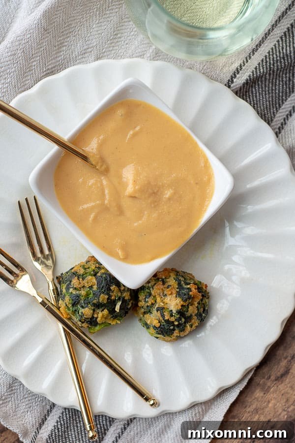 Two golden-brown spinach balls presented on a white plate, accompanied by elegant gold forks.