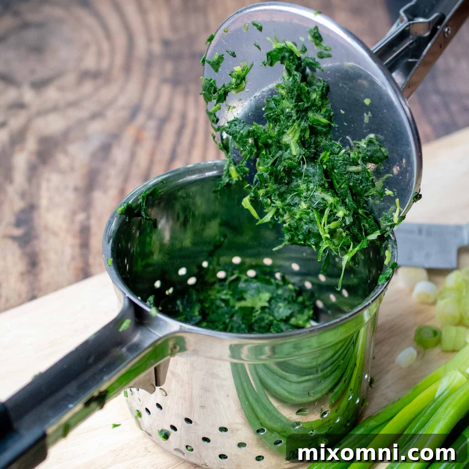 Chopped frozen spinach being squeezed dry in a potato ricer, demonstrating a key step for perfect spinach balls.