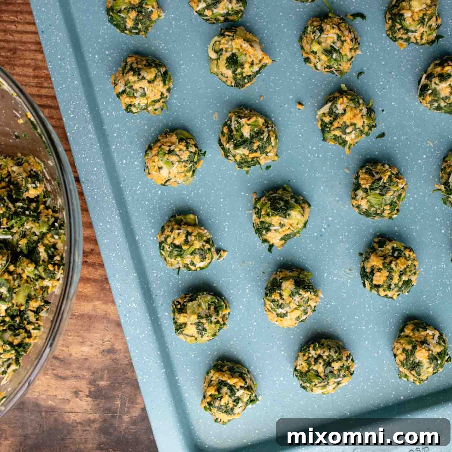 Unbaked spinach balls perfectly portioned and arranged on a baking sheet, ready for the oven.