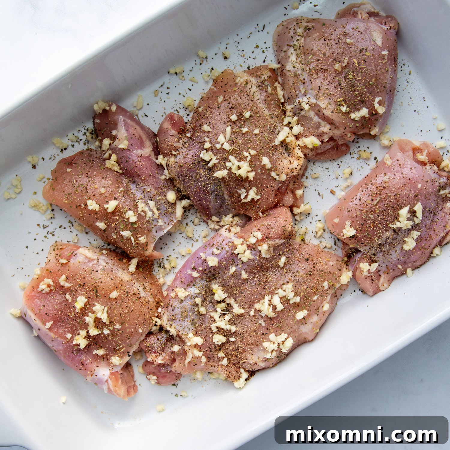 raw chicken with minced garlic, salt, pepper, and Italian seasoning sprinkled on top in a baking dish.