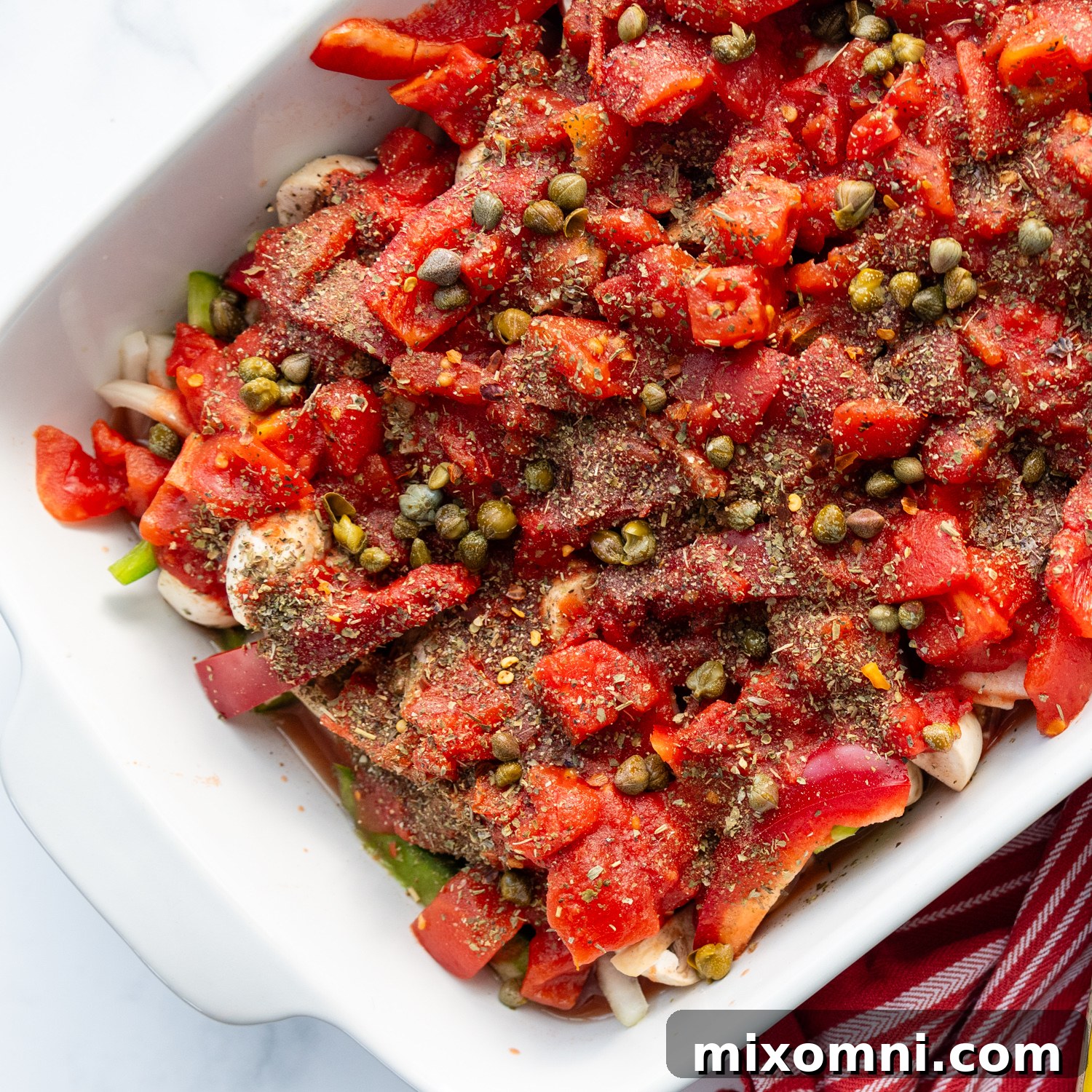 crushed and diced tomatoes, seasonings, and capers layered over chicken and vegetables before going into the oven.