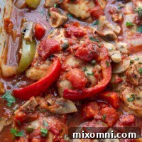 close up of baked chicken with peppers, mushrooms, and onions in a tomato sauce