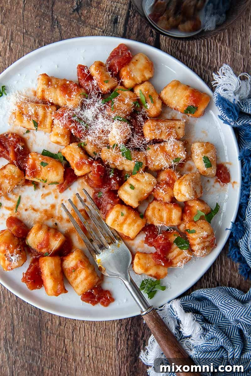 Overhead shot of freshly cooked gluten-free ricotta gnocchi served on a white plate, generously coated in vibrant red sauce, ready to be enjoyed.