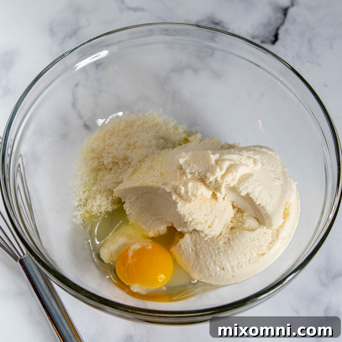 All the wet ingredients for gluten-free gnocchi, including ricotta, egg, olive oil, and parmesan, are shown in a mixing bowl before flour is added.