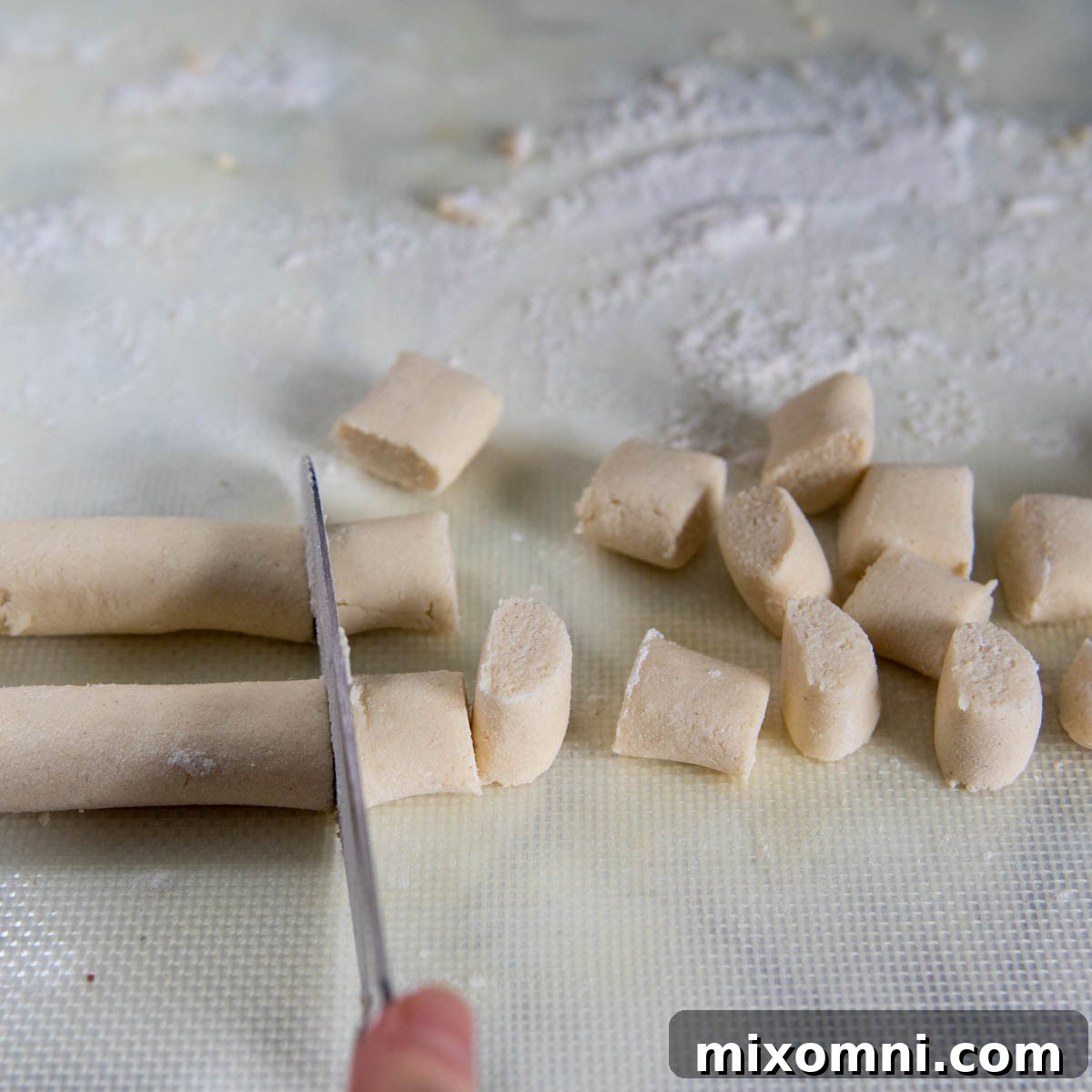 Two long ropes of gluten-free gnocchi dough rolled out on a floured surface and being cut simultaneously into uniform ½-inch pieces.