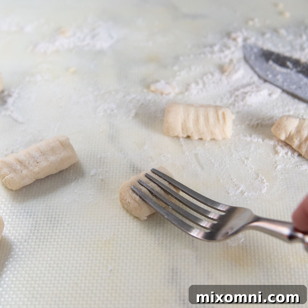 A fork pressing into a piece of gluten-free gnocchi dough to create traditional ridges, enhancing its ability to hold sauce.