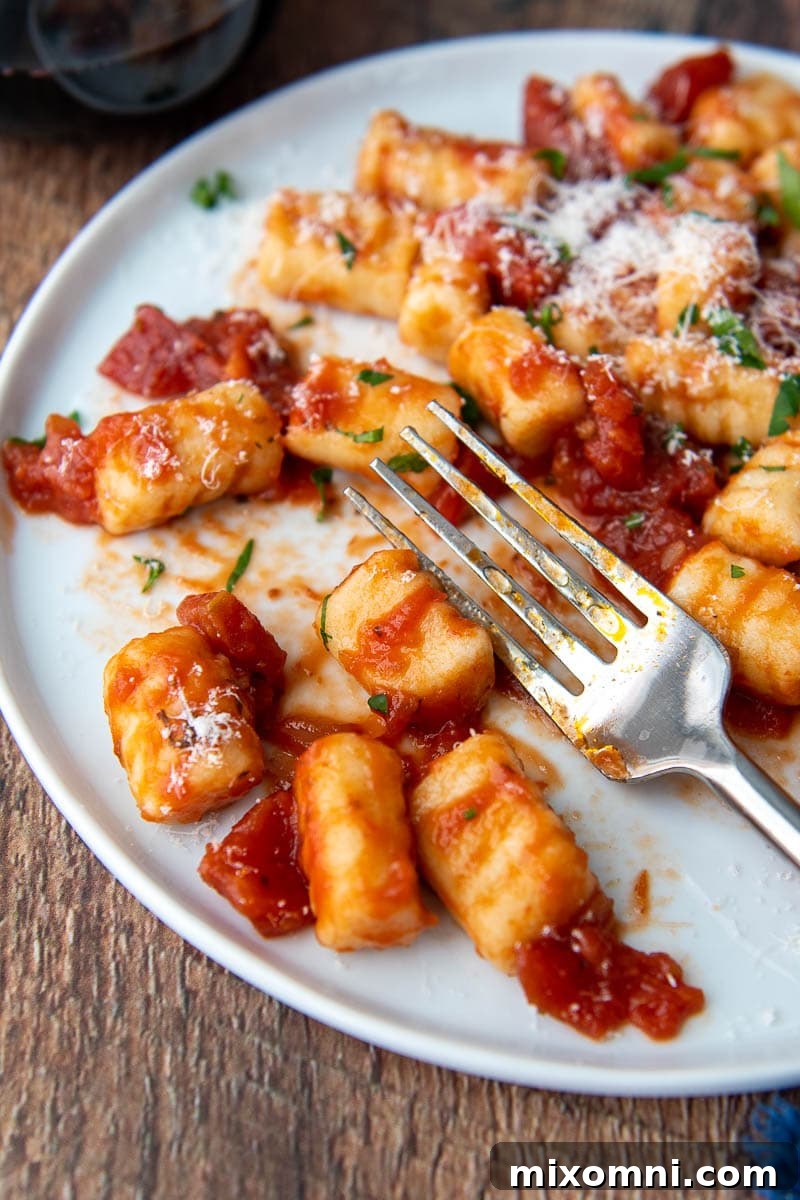 Close-up of a fork resting on a plate of perfectly cooked gluten-free ricotta gnocchi, lightly sauced and ready for a delicious meal.