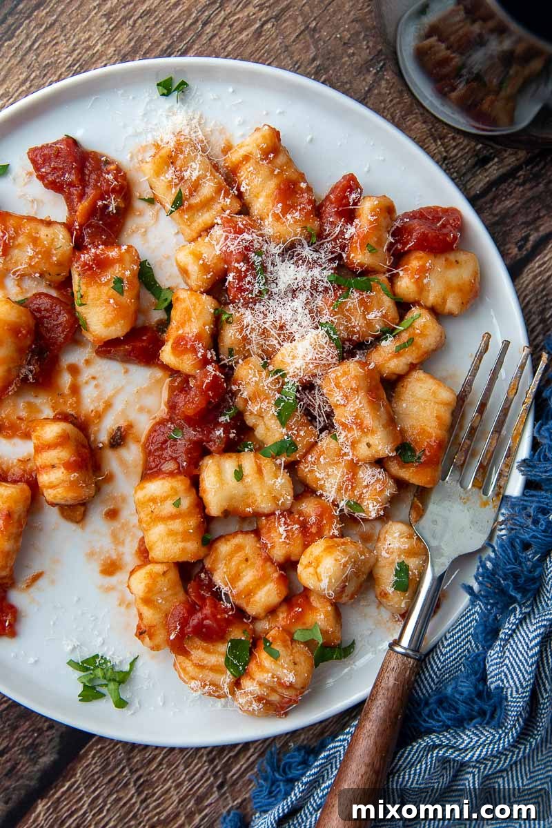 Overhead shot of freshly prepared gluten-free ricotta gnocchi on a clean white plate with a fork resting beside it, highlighting its inviting texture.