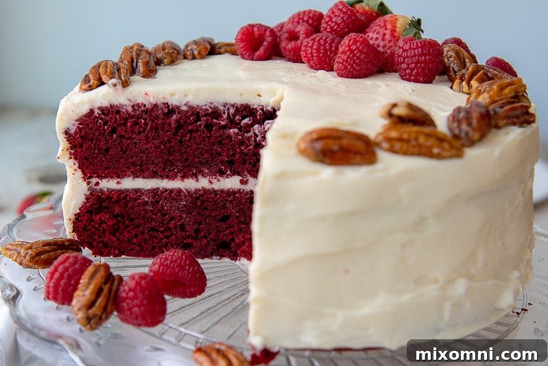 a cut red velvet cake on a glass platter with fresh berries around