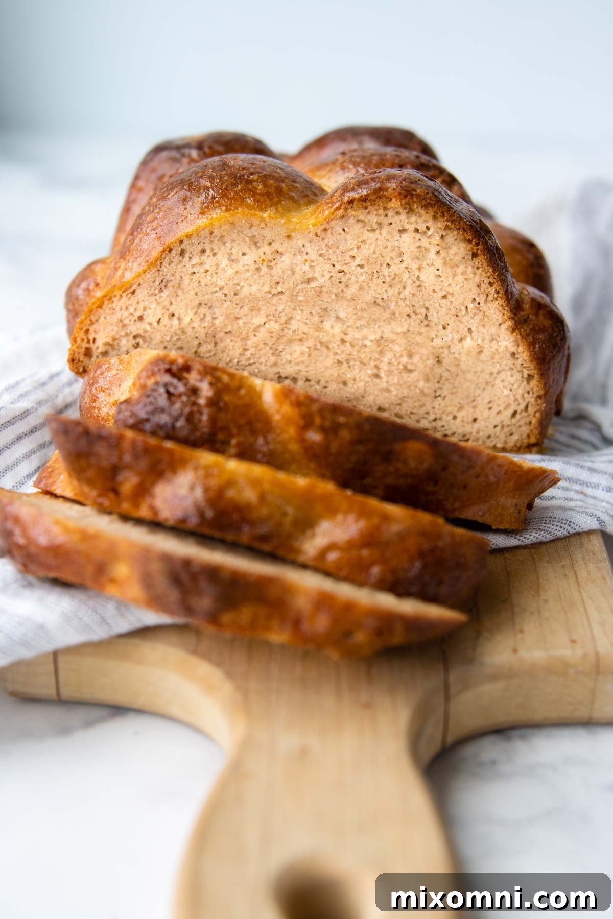 A beautifully sliced loaf of golden-brown gluten-free challah bread resting on a white towel, showcasing its soft, airy interior.