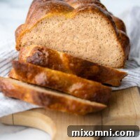 A beautifully sliced loaf of golden-brown gluten-free challah bread resting on a white towel, showcasing its soft, airy interior.