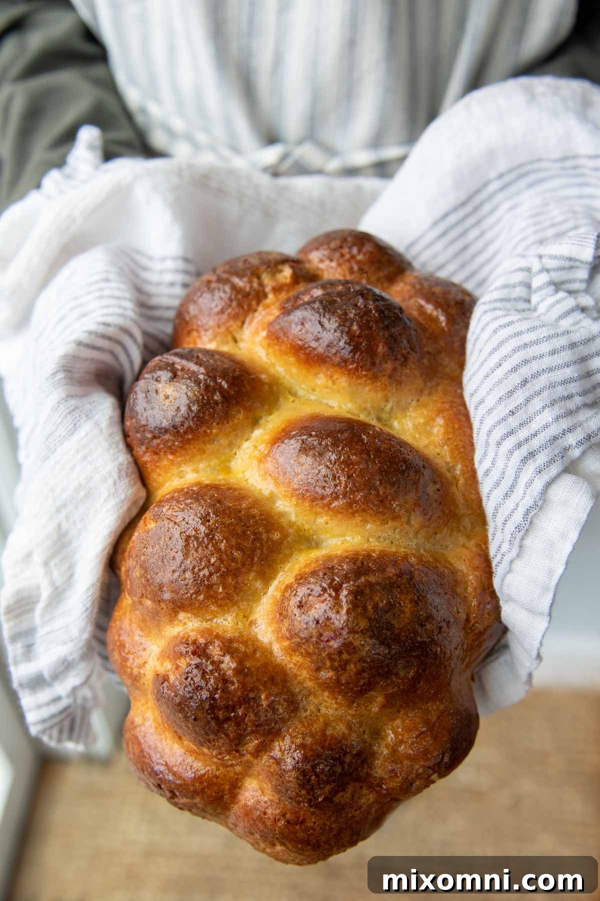 A freshly baked, uncut loaf of golden gluten-free challah bread held by someone wearing an apron, highlighting its perfect crust.