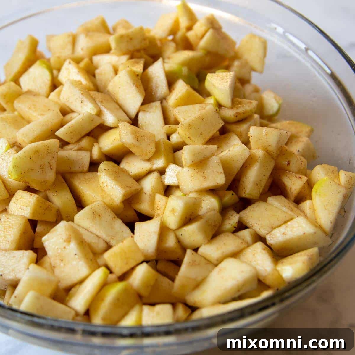 Freshly chopped Golden Delicious apples glistening in a large glass mixing bowl, coated with cinnamon and sugar, ready for the cobbler filling.