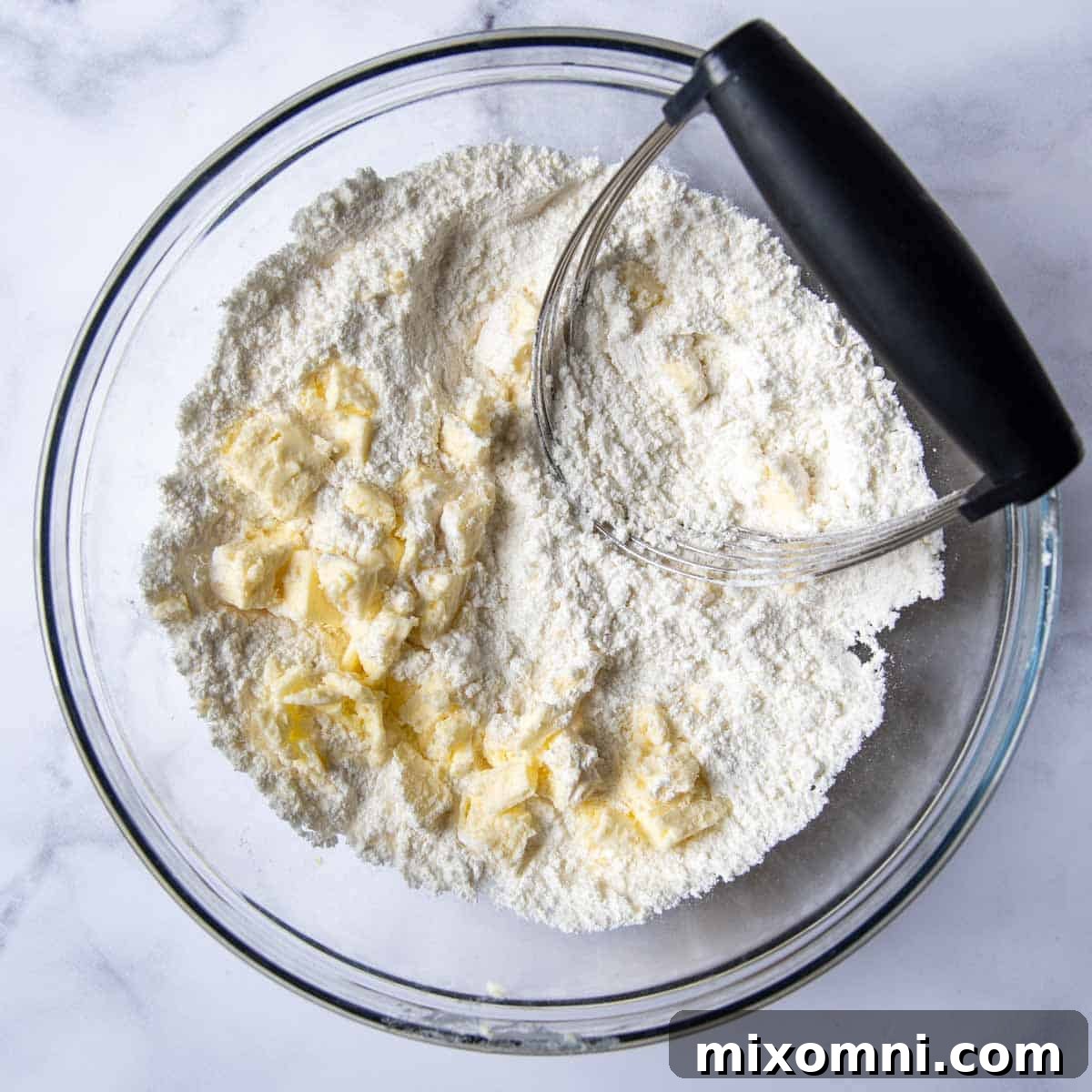 A pastry blender meticulously cutting cold butter into a bowl of gluten-free flour mixture, demonstrating the technique for a tender biscuit topping.