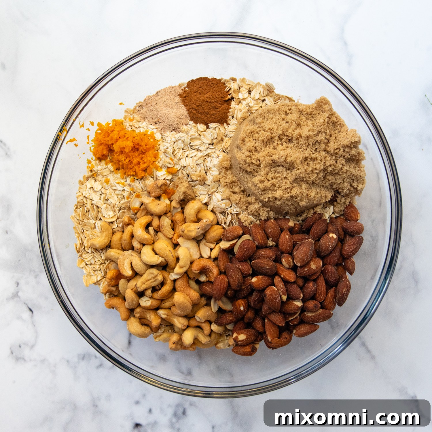 All the dry ingredients for granola, including oats, nuts, and spices, gathered in a large mixing bowl.