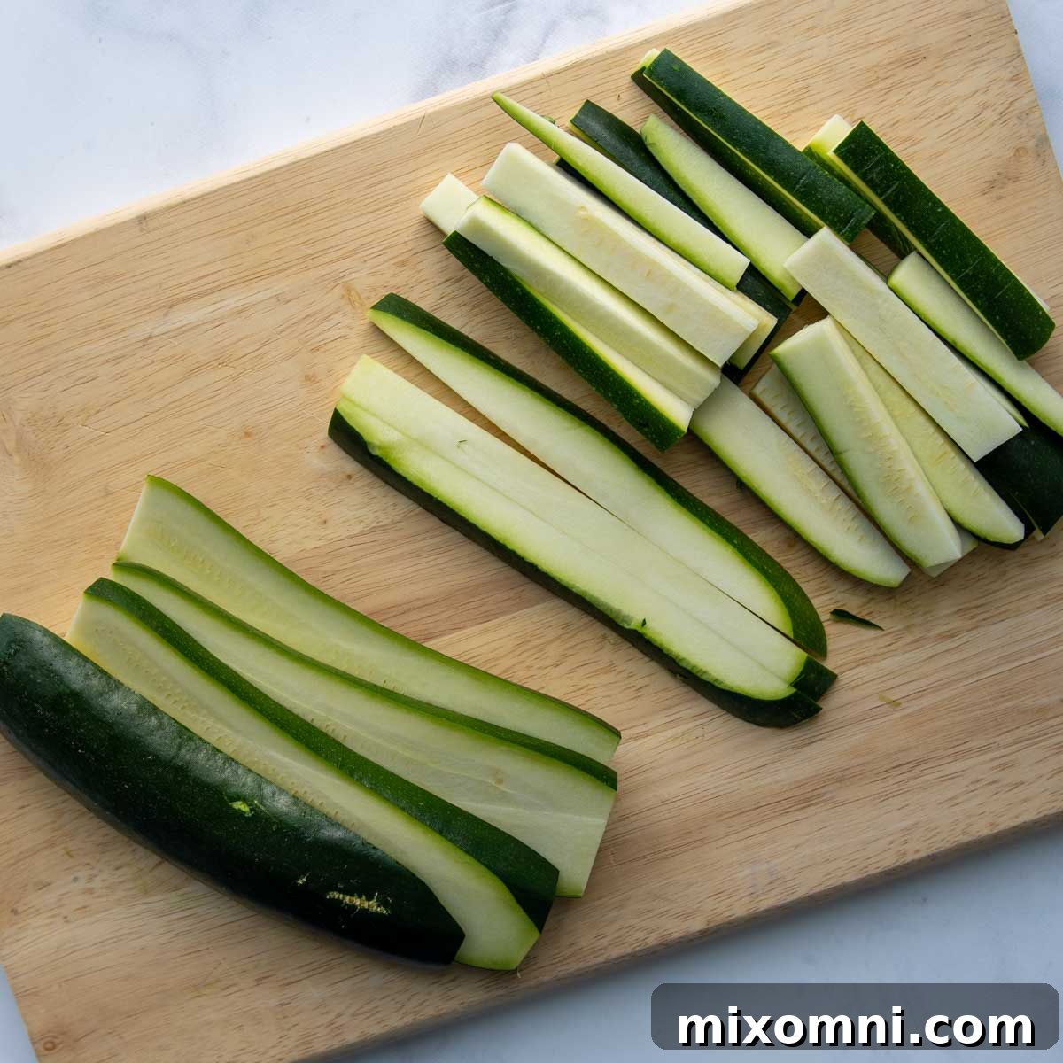 Fresh zucchini expertly cut into uniform sticks, ready for breading and baking.