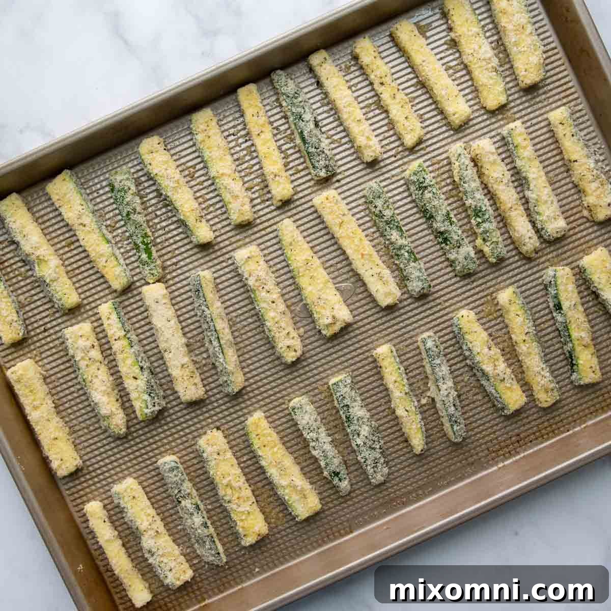 Unbaked, breaded zucchini sticks neatly arranged on a greased baking sheet, with ample space for crisping.