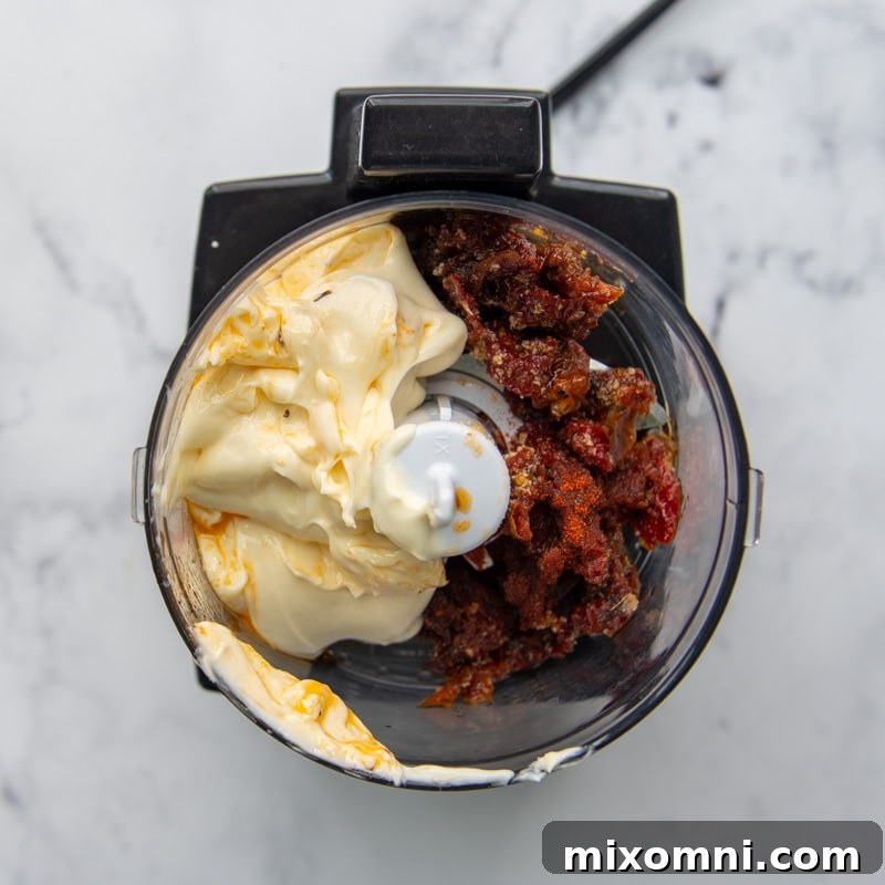 Overhead shot of a vibrant sun-dried tomato aioli blending smoothly in a mini food processor.