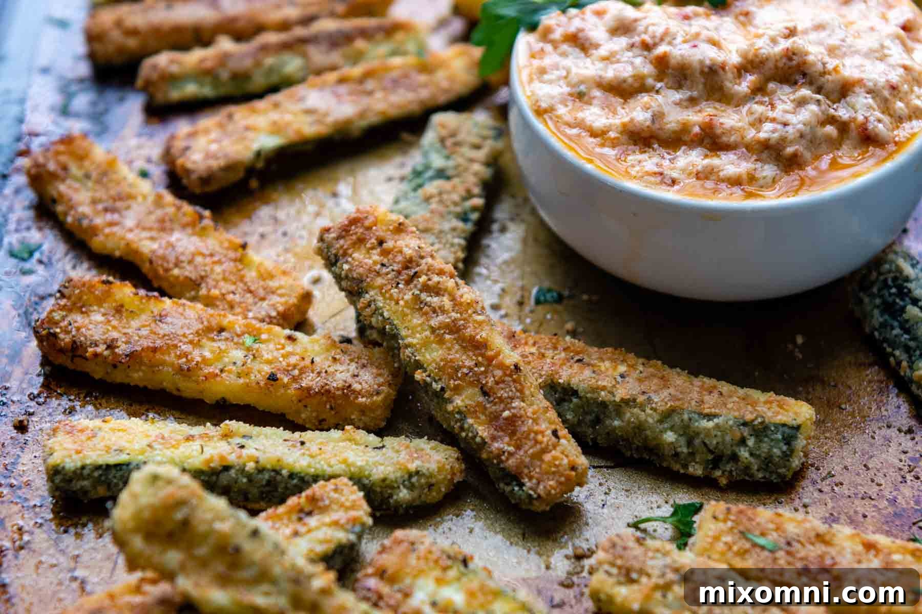 A vibrant shot of crispy zucchini fries piled high, with a cup of sun-dried tomato aioli in the background, ready for dipping.