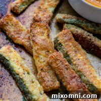 Close-up of baked zucchini fries on a baking sheet with dip in background