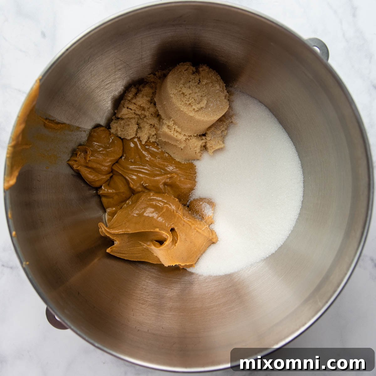 Creamy peanut butter, granulated sugar, and brown sugar mixed in a bowl, ready for the next step of cookie preparation.