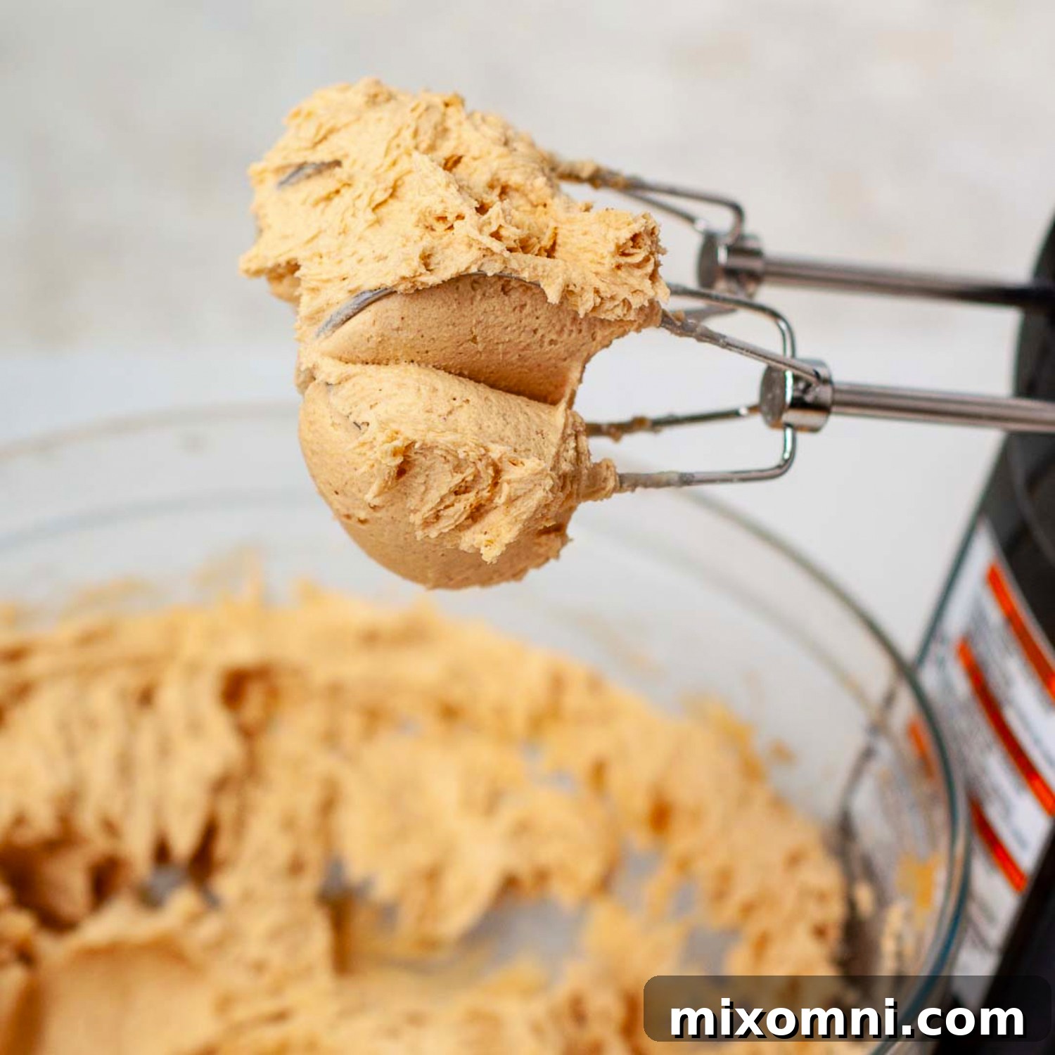 Creamy peanut butter mixture on a beater, showcasing its thick, smooth texture, ready to be spread over the caramel layer.