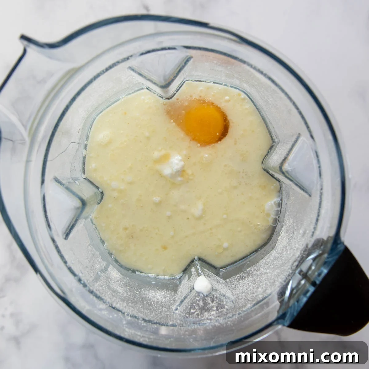 Wet ingredients like egg and milk being added to the blender with oat flour.